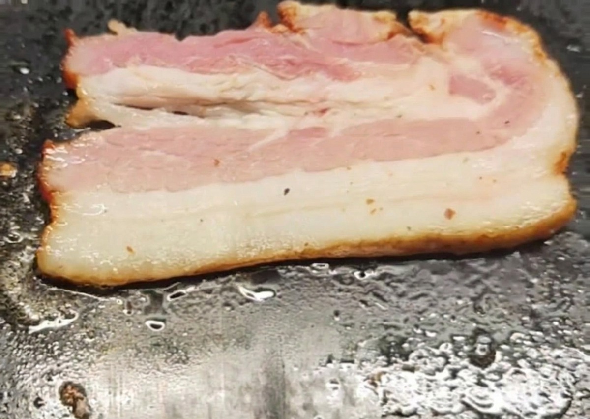 A single strip of bacon sizzling and frying on a hot, flat griddle surface.
