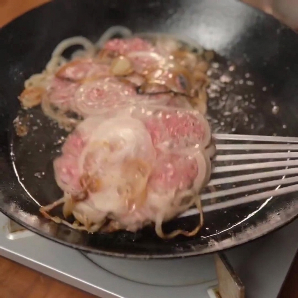 A freshly cooked smash burger patty topped with melted cheese being placed onto a toasted bun.