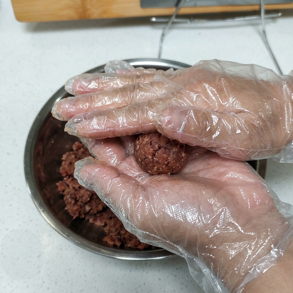 Gloved hands holding and pressing a ball of seasoned ground beef into a patty shape.