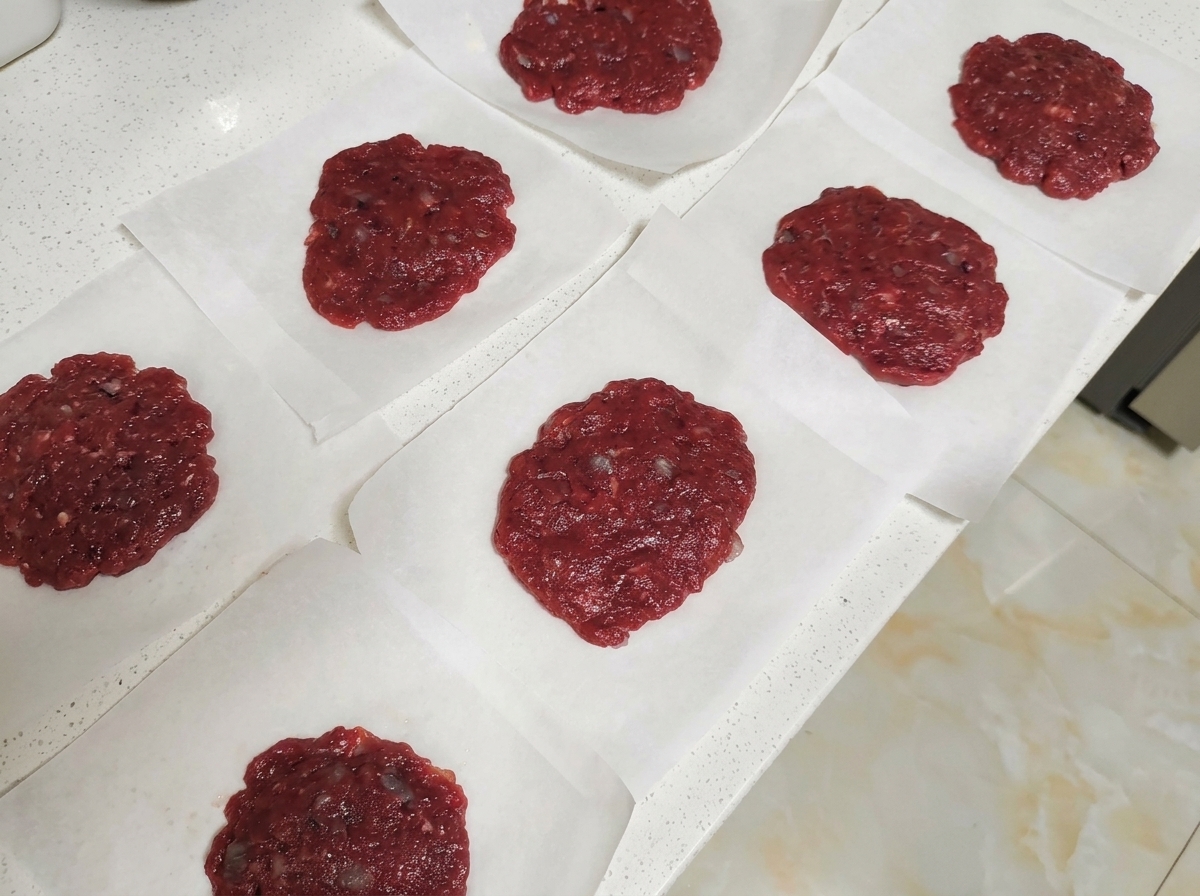 Several raw round beef patties placed individually on squares of white parchment paper on a light countertop.