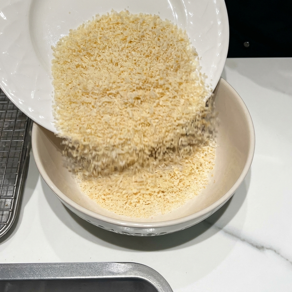 A bowl containing breadcrumbs, grated Parmesan cheese, and various spices being mixed.