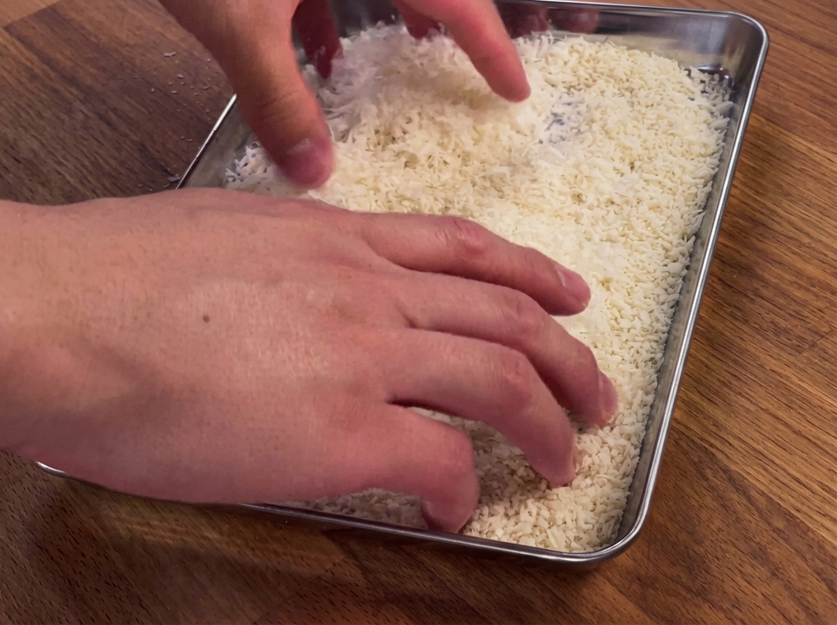 Hands pressing a chicken breast into a tray of breadcrumbs and parmesan cheese.