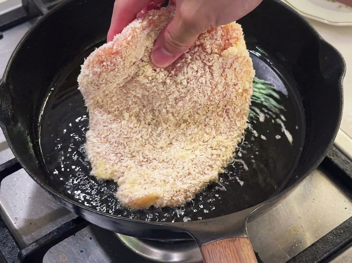 Breaded chicken breast frying in a pan with hot oil.