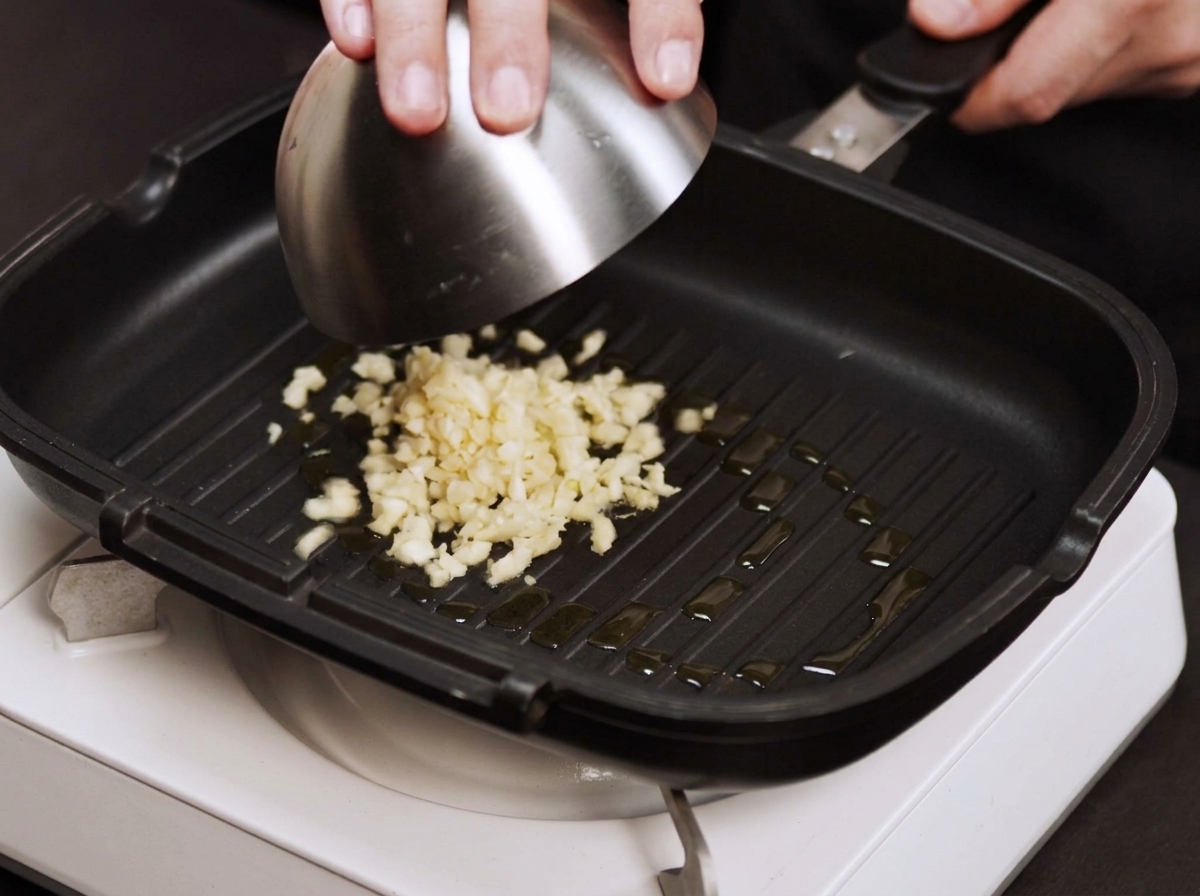 Finely chopped garlic and onion pieces sizzling in a hot, lightly oiled grill pan.