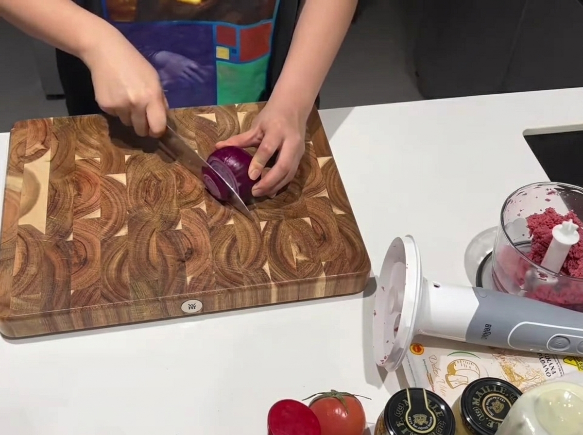 A sharp kitchen knife slicing through a fresh red onion on a wooden cutting board.
