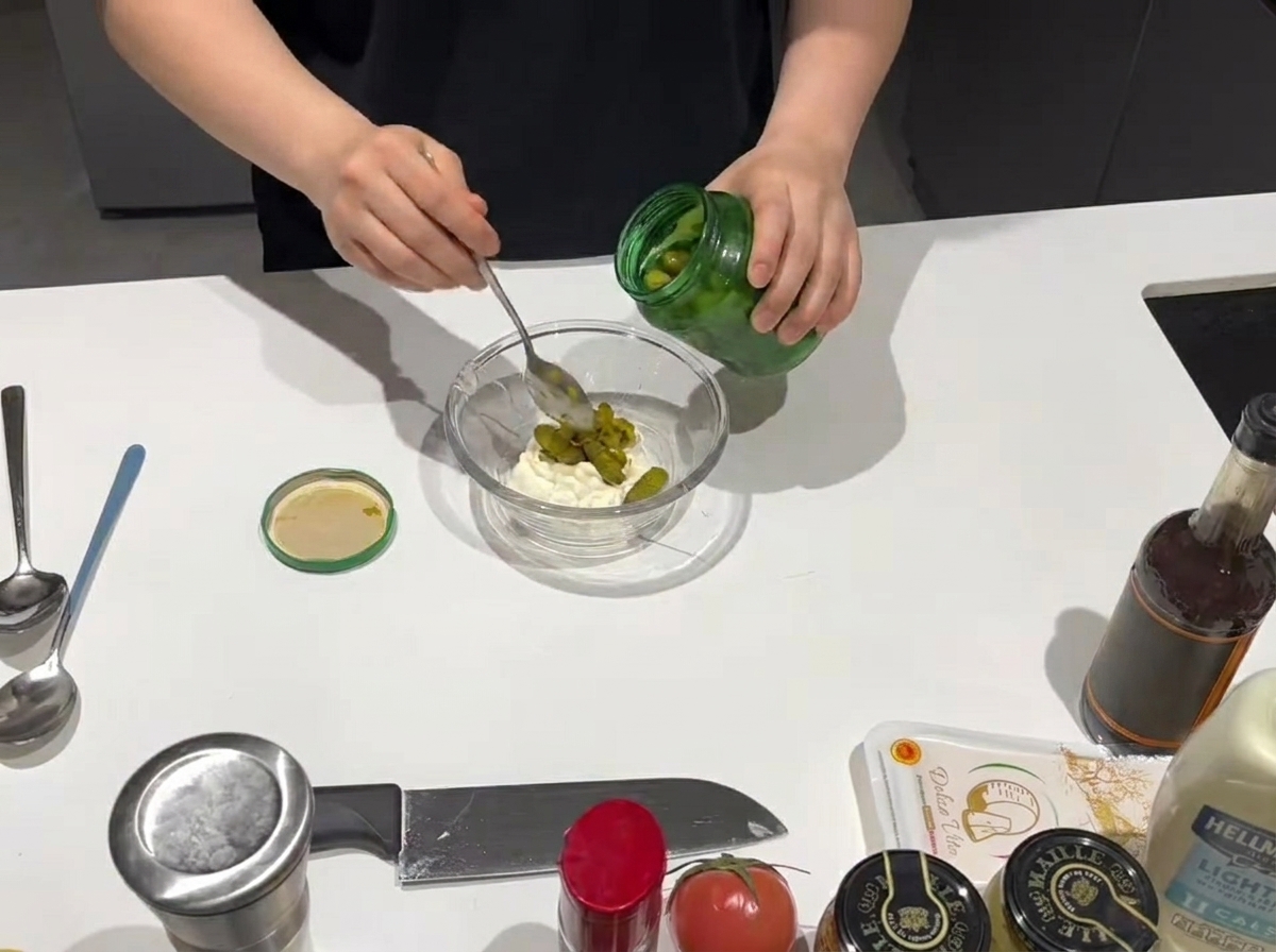 A spoonful of sweet relish being added to a bowl of creamy mayonnaise.