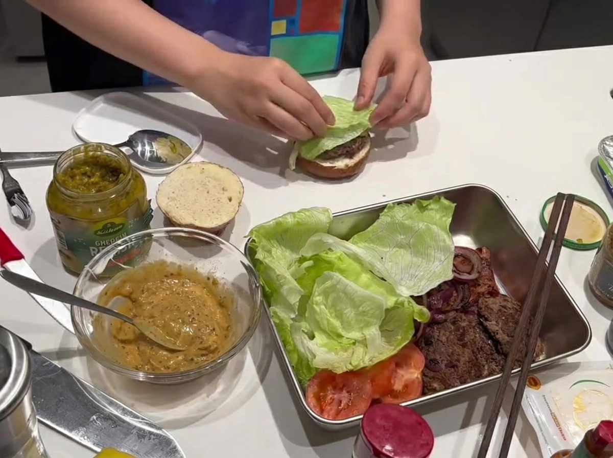 A crisp lettuce leaf being placed on a cooked beef patty.