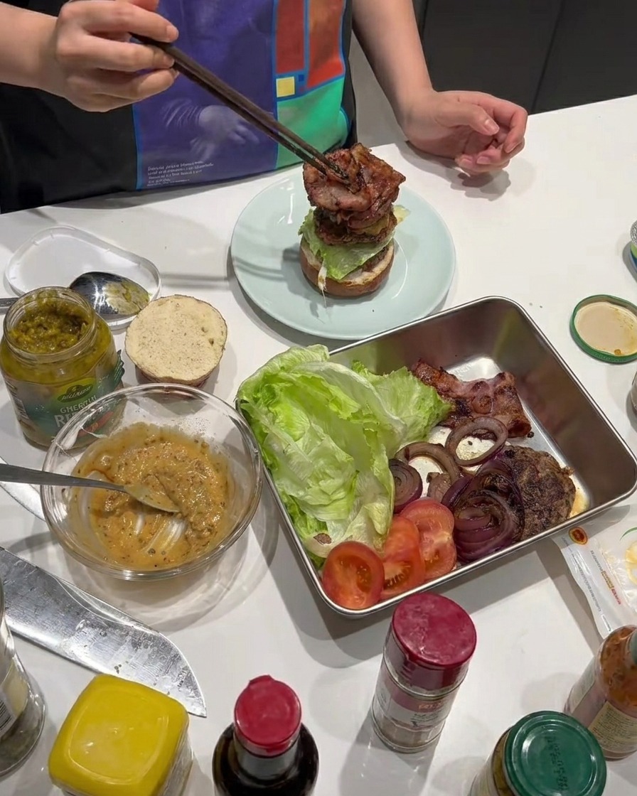 Crispy cooked bacon strips being added to the burger assembly.