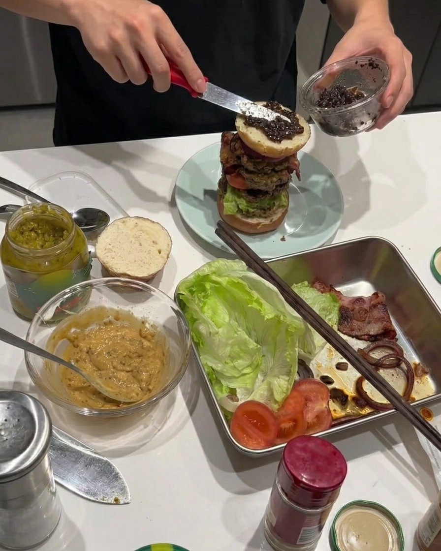 Black truffle paste being spread across the fried onion rings on the stacked burger.