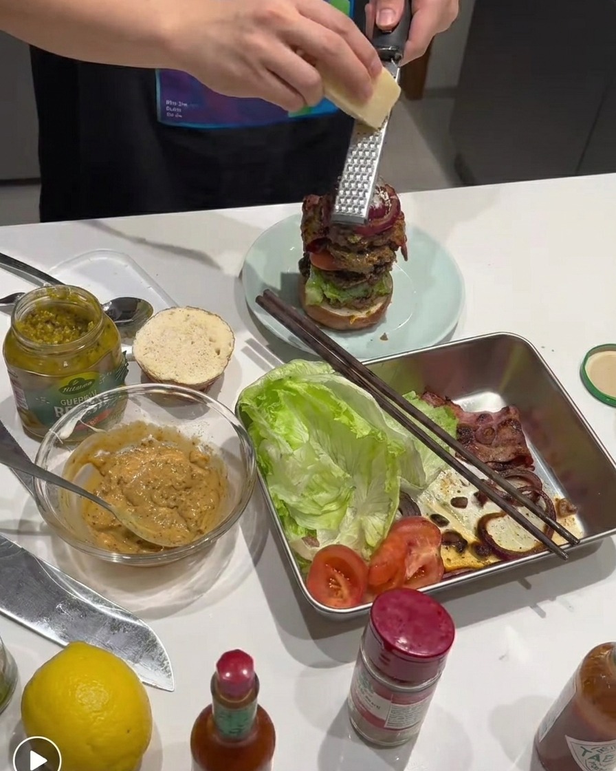 Fresh Parmesan cheese being grated onto the layered burger stack.