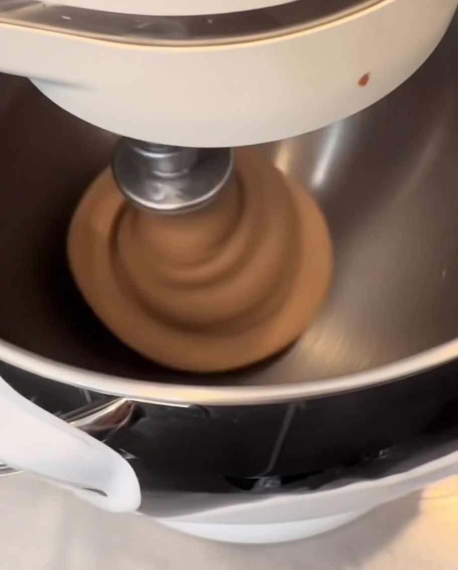 Dark cocoa-infused dough being shaped into smooth, round balls on a silicone mat.