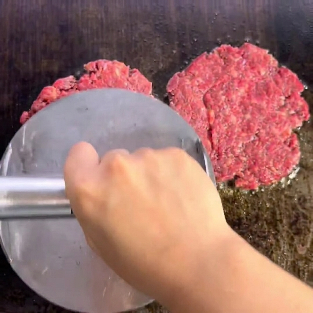 Two seasoned beef patties sizzling on the grill, showing a browned and seared crust.