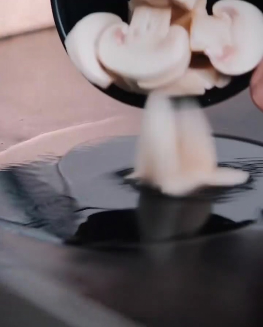 Fresh mushroom slices cooking on a hot flat-top grill.