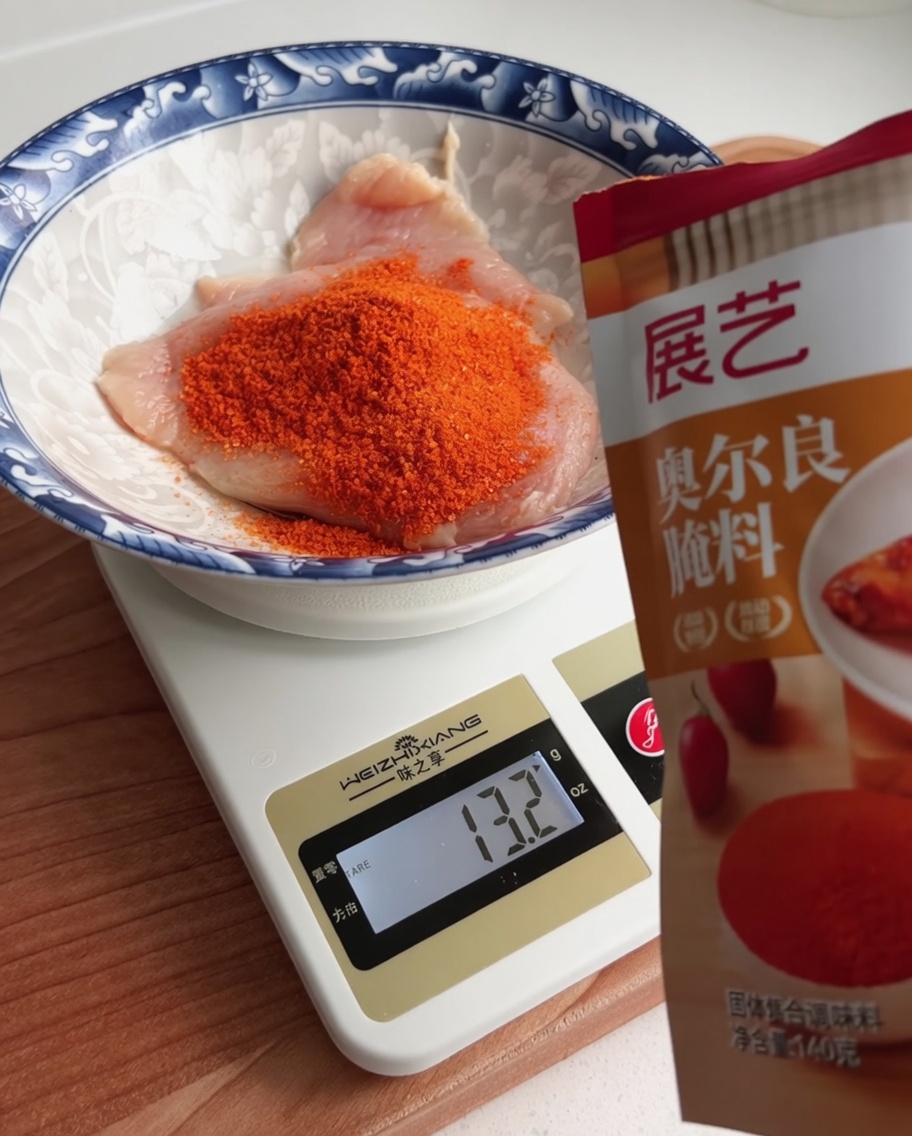 Orleans marinade powder being weighed out into a bowl containing a piece of raw chicken.