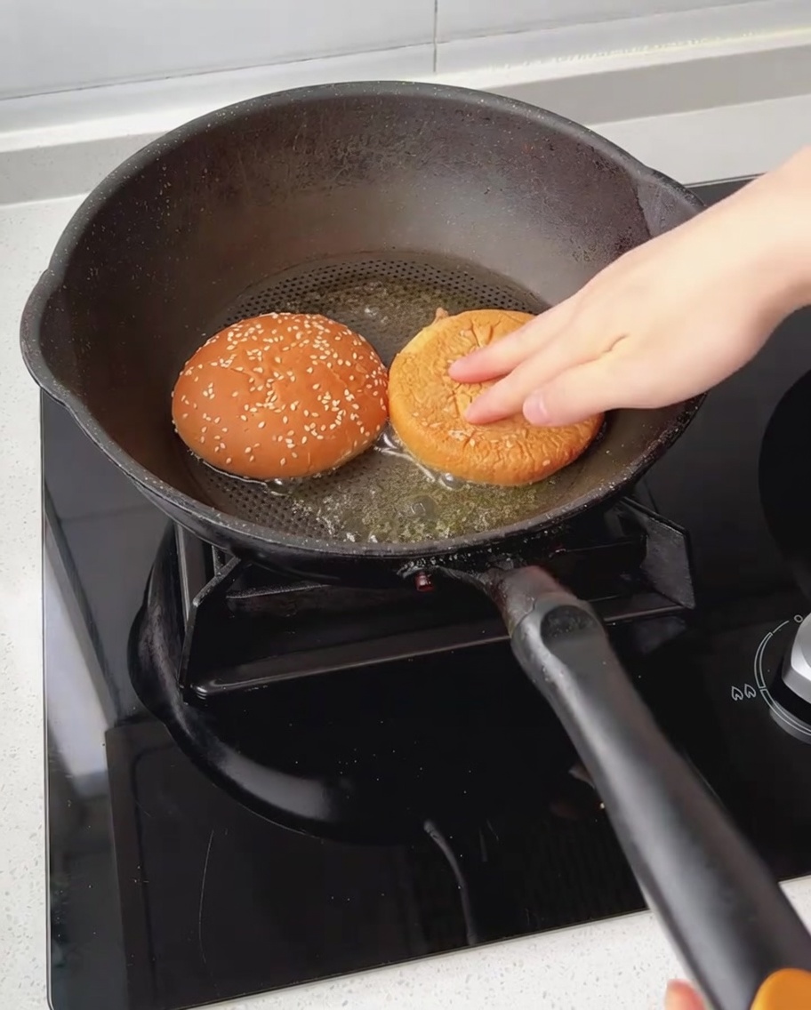 Burger bun halves being toasted face-down in a pan with melted butter.
