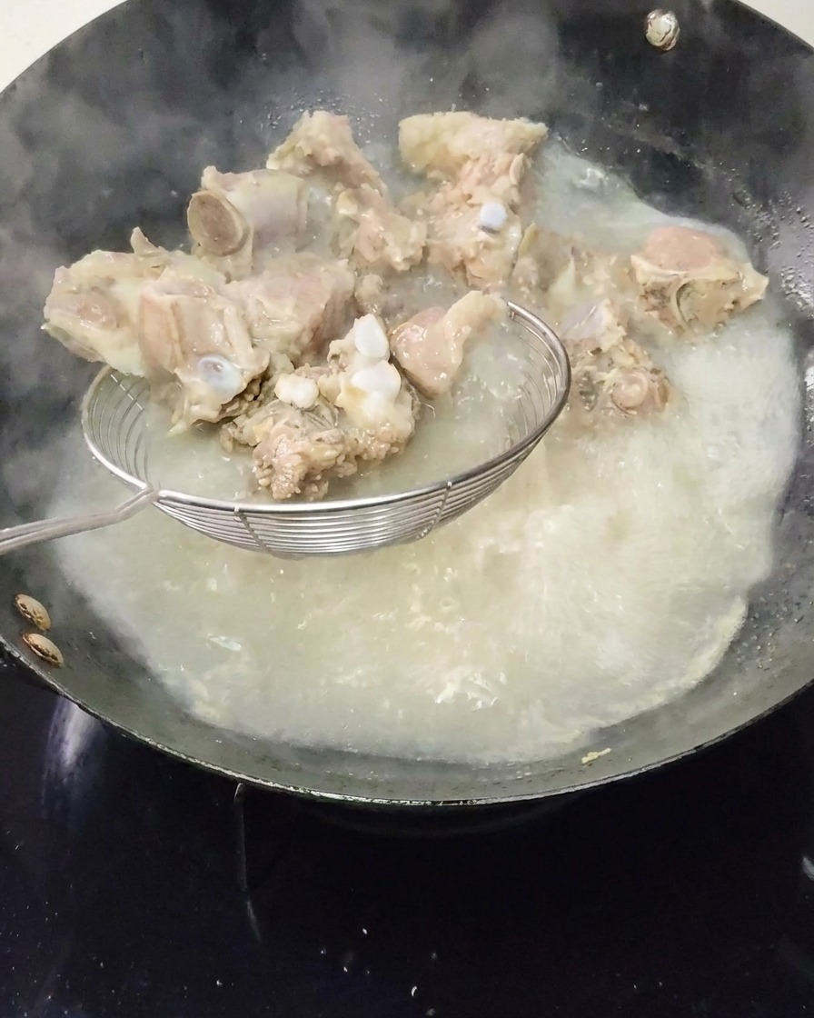 Blanched pork ribs being lifted out of boiling water using a wire spider strainer.