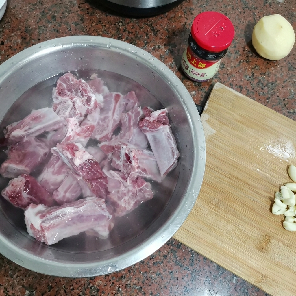 Raw pork ribs submerged in a large metal bowl filled with cold water.