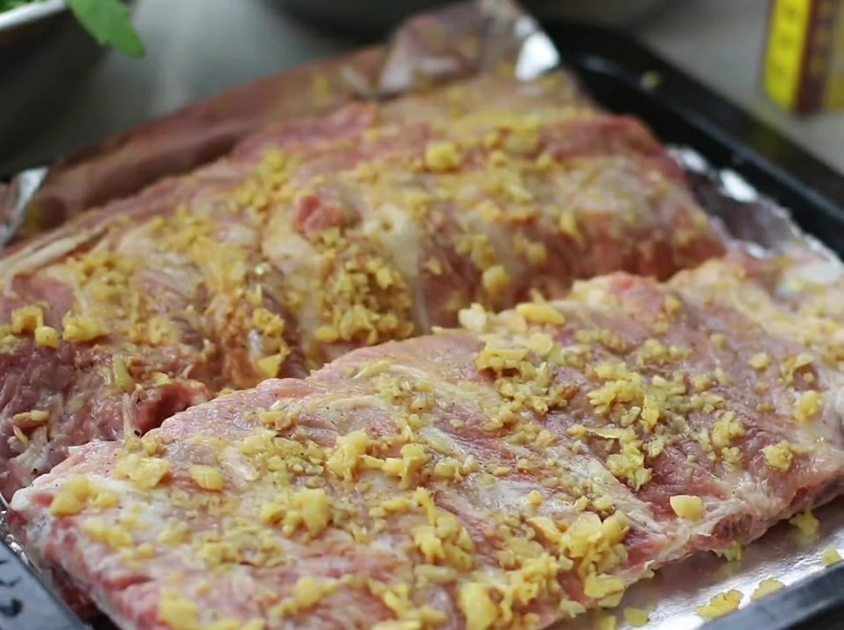 A roasting tray containing seasoned pork ribs, tightly wrapped with a layer of shiny aluminum foil.