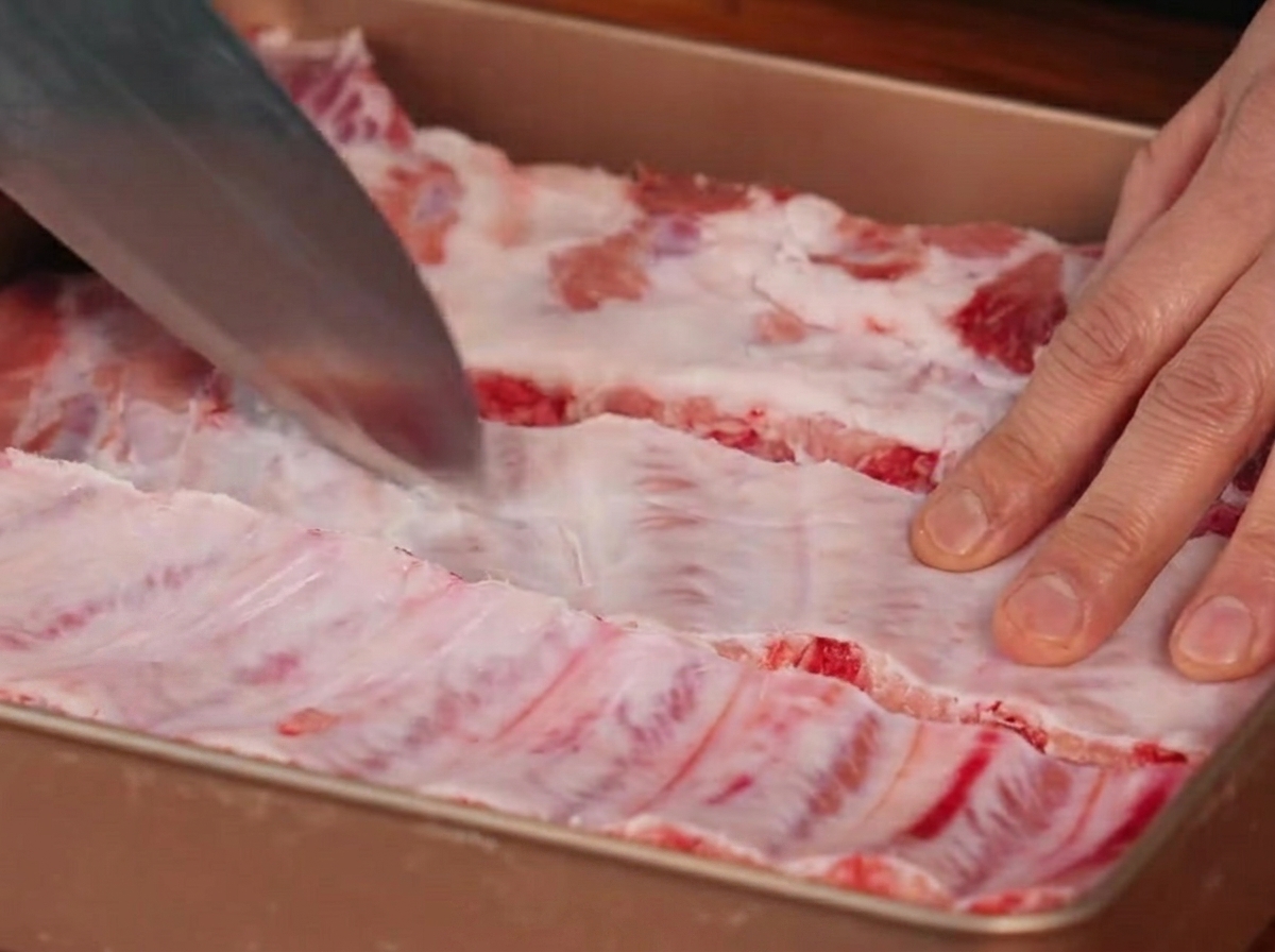 A knife making incisions into the membrane located on the back of the pork ribs.