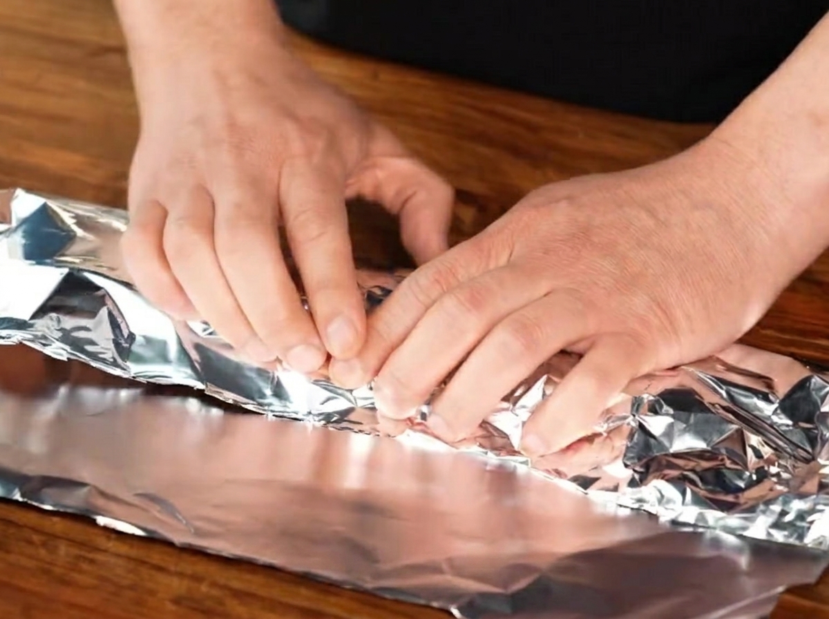 Seasoned pork ribs being tightly enclosed within a sheet of aluminum foil.