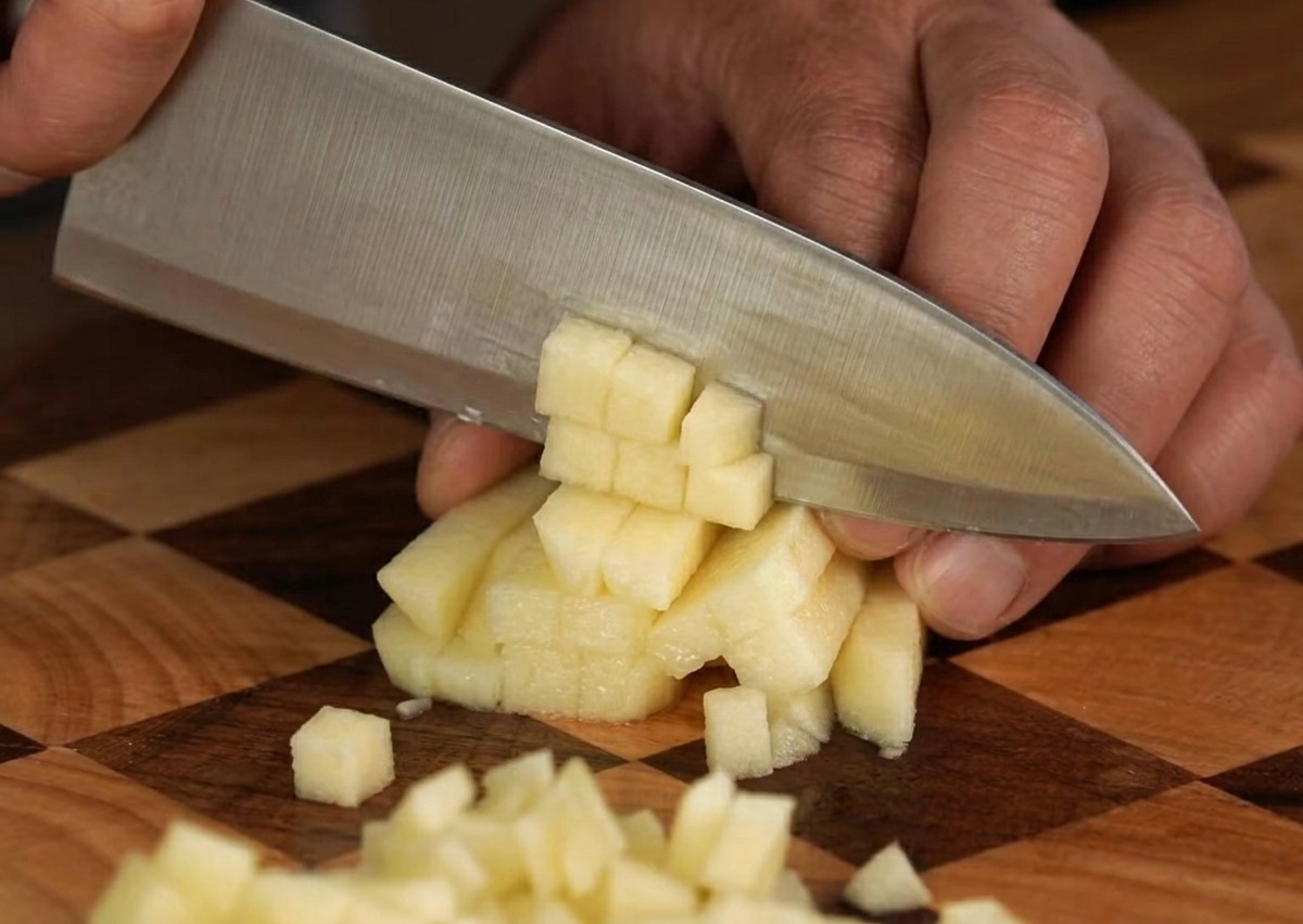 Fresh apple being carefully diced into small, uniform cubes on a wooden cutting board.