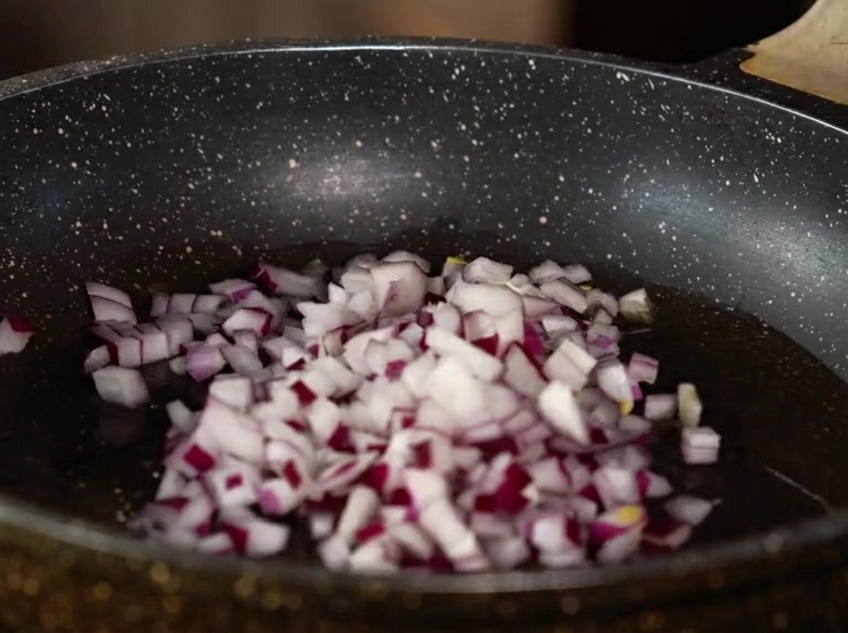 Diced red onion, minced garlic, and ginger cooking in a pan with oil.