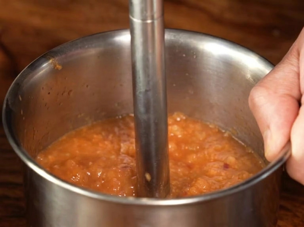 A metal hand blender processing the cooked sauce mixture into a smooth puree.