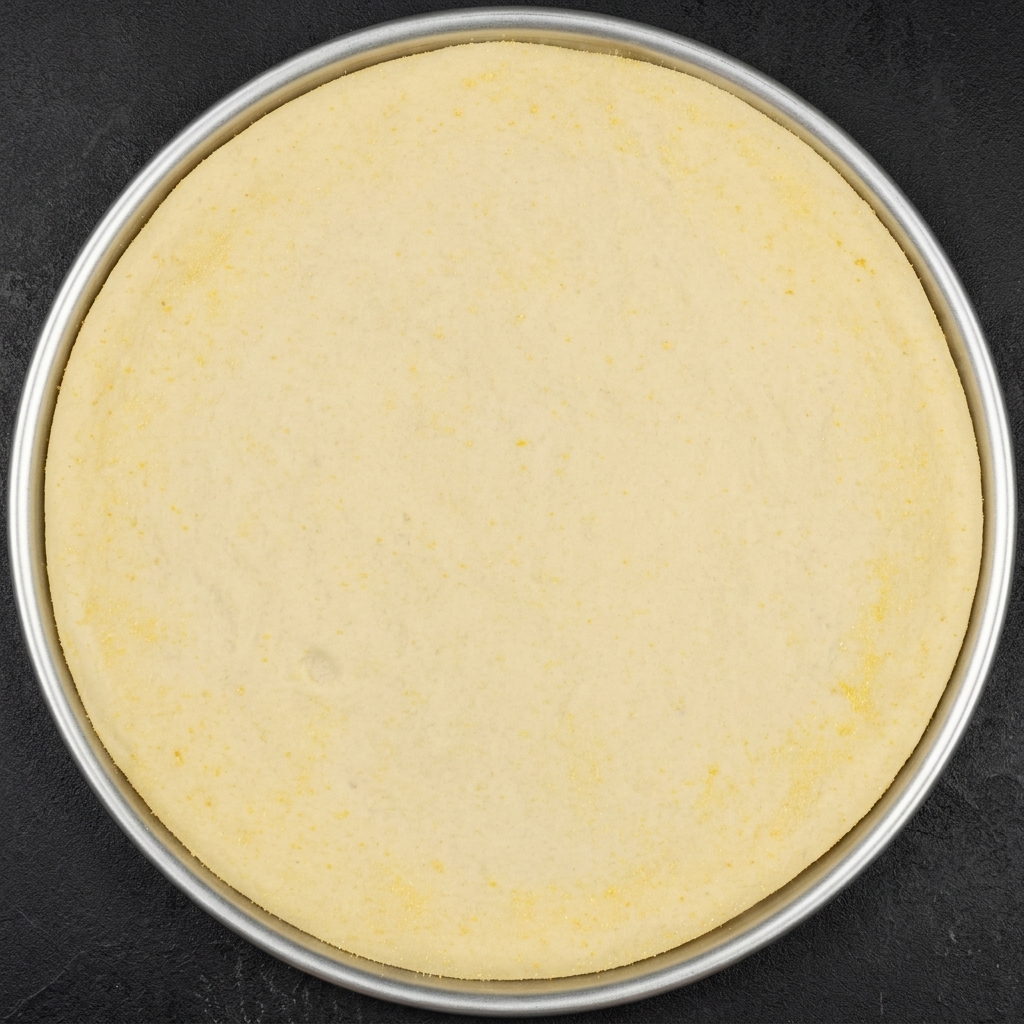 A round piece of proofed pizza dough inside a metal pan, with multiple radial cuts made along the outer edge.