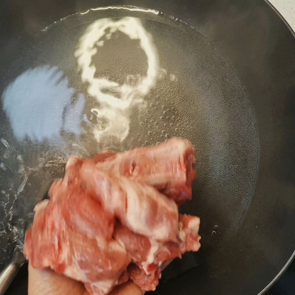Pork ribs being blanched in a pan of boiling water with cooking wine, showing foam rising to the surface.