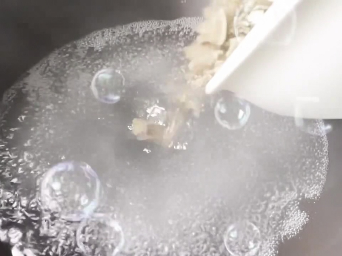 Clams being poured into a pot of boiling water with aromatics.