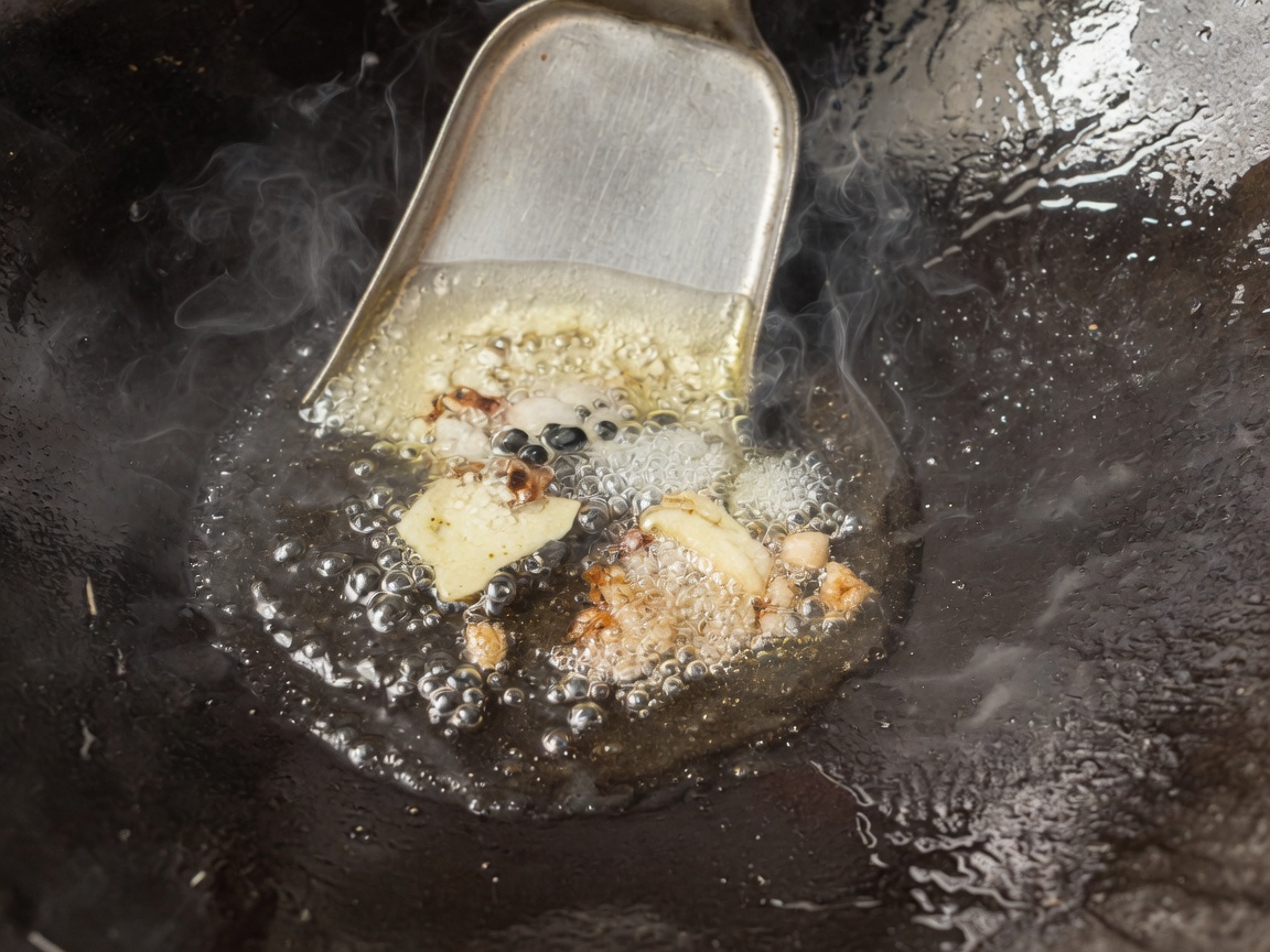 Aromatics and spices sizzling in hot oil inside a seasoned wok.