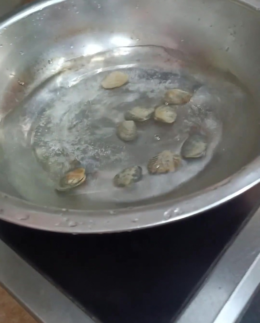 Clams cooking in a pot of boiling water, with some shells beginning to open.