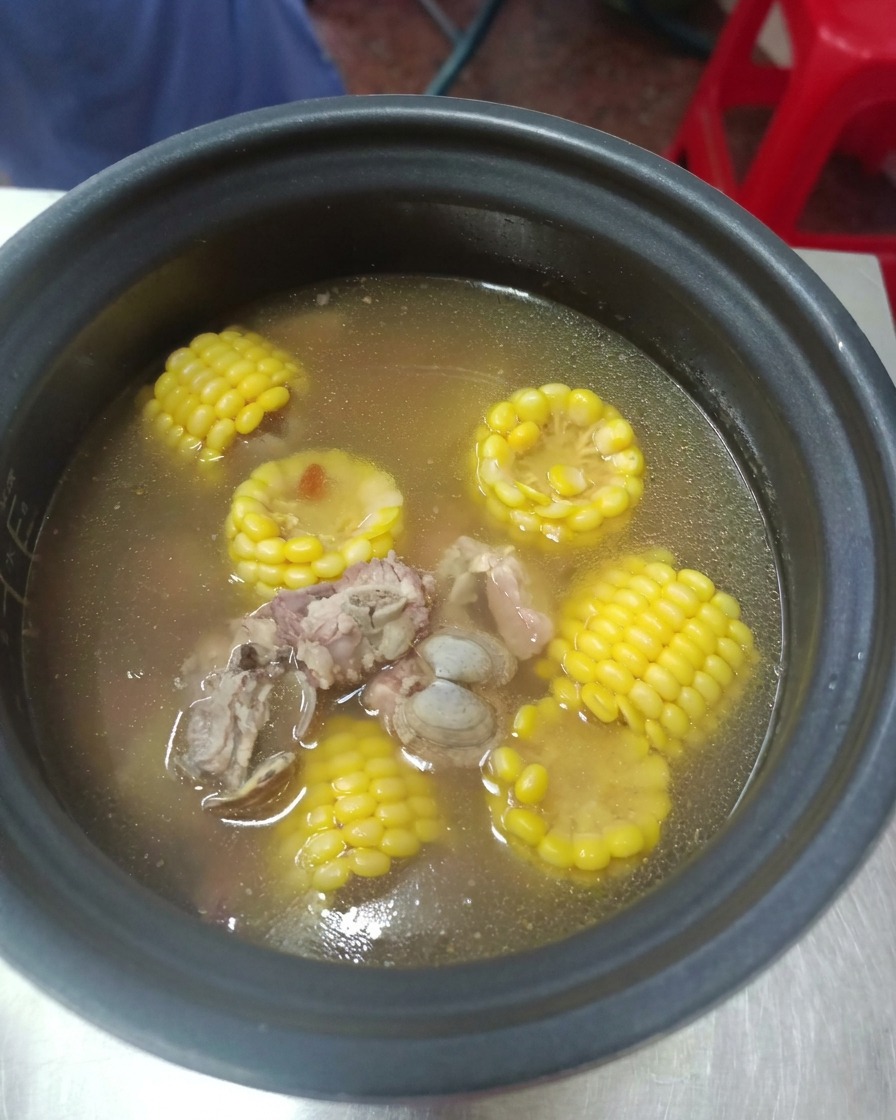A safely opened pressure cooker revealing a steaming hot clear broth with tender pork ribs and bright yellow corn.