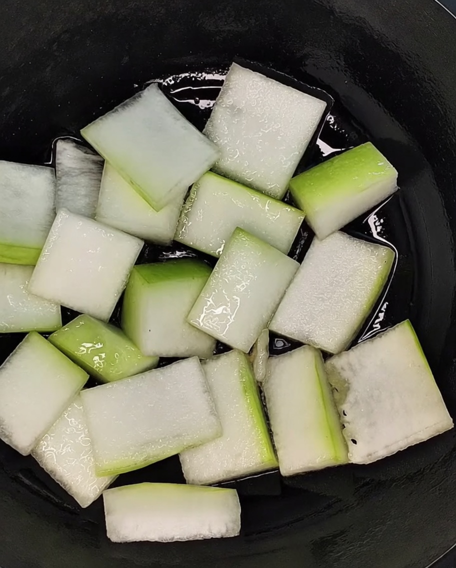 Pieces of sliced winter melon arranged evenly to cover the bottom of a black pot.