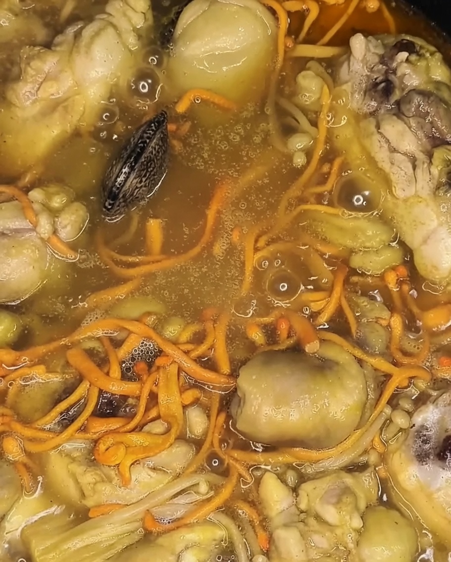Fresh clams being added to the simmering pot, resting on top of the cooked chicken and vegetables.