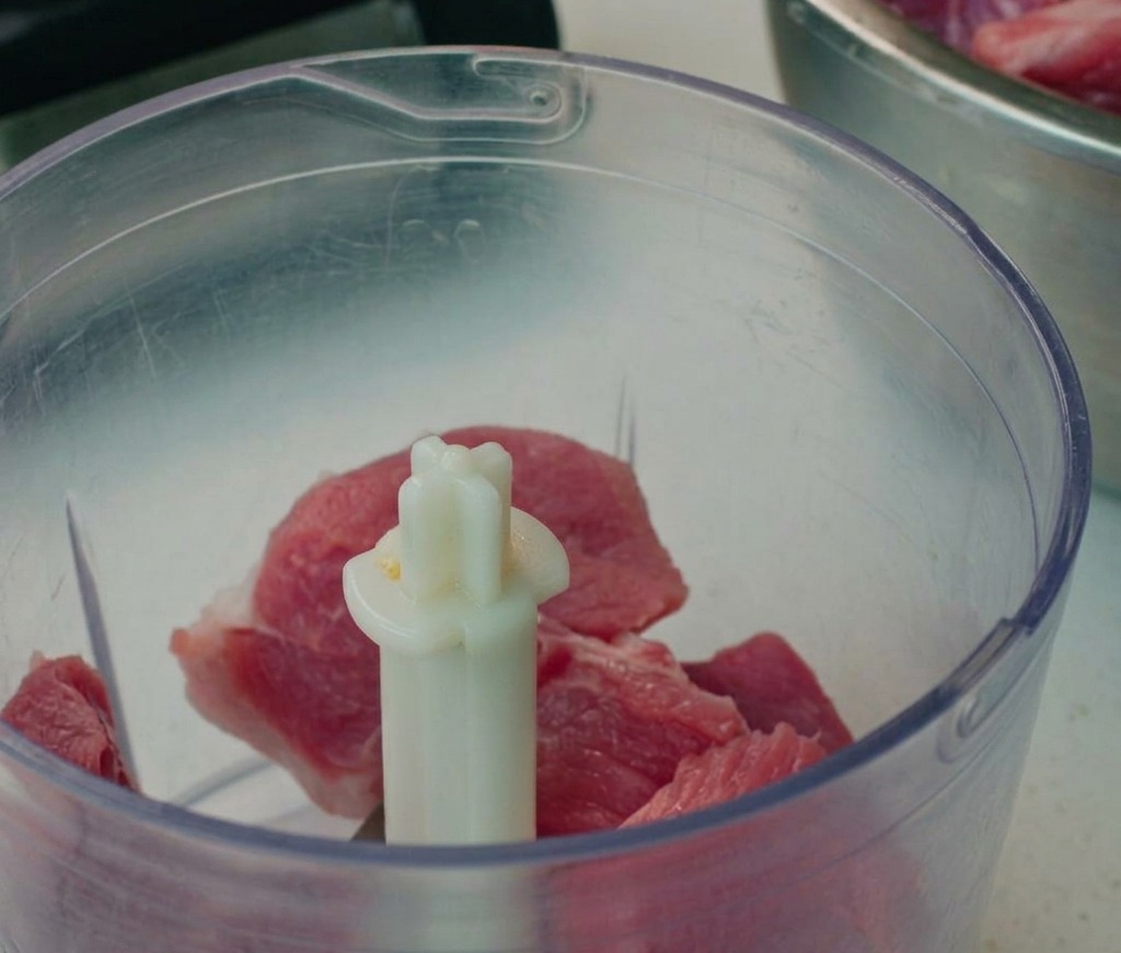 Ground pork pieces inside a food processor bowl.