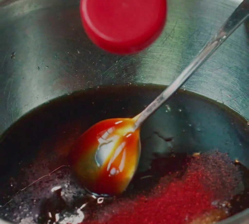 Ground pork being mixed with various liquid seasonings in a stainless steel bowl.