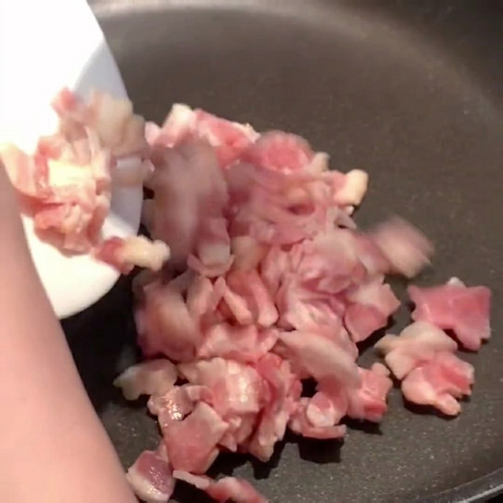 Bacon pieces sizzling in a hot pan, releasing golden rendered fat.