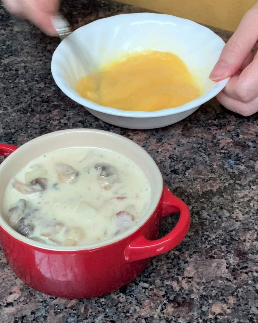 A round sheet of puff pastry being placed to cover a small red soup bowl.