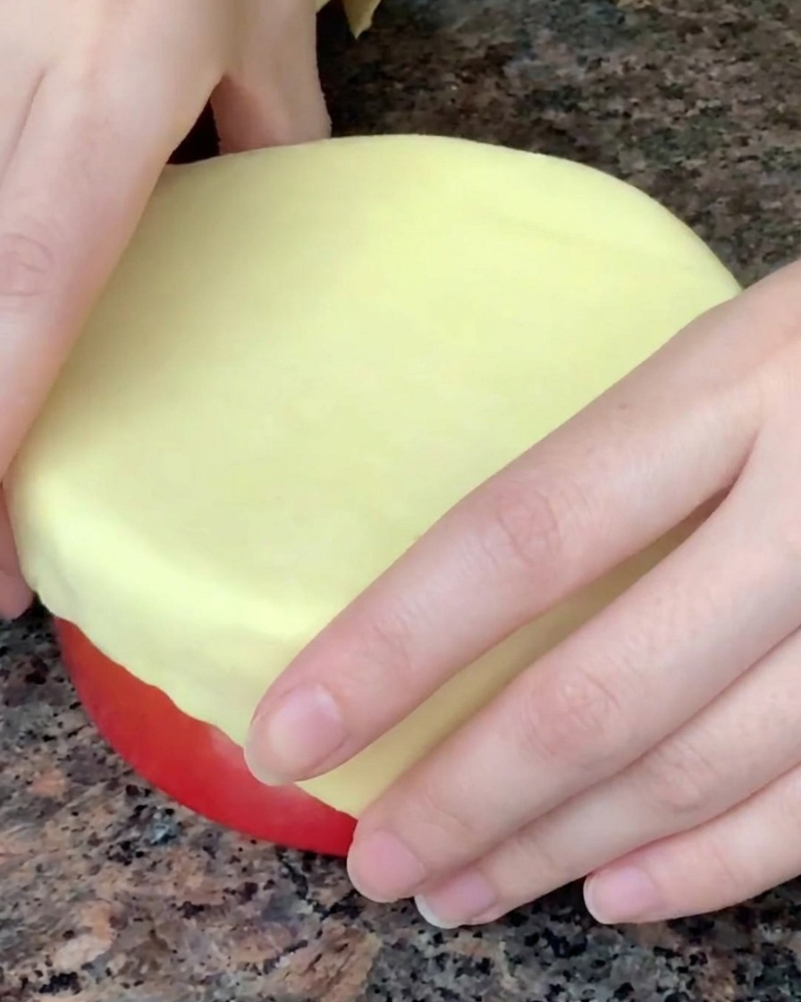 Egg wash being brushed onto the top of puff pastry covering a red soup bowl.