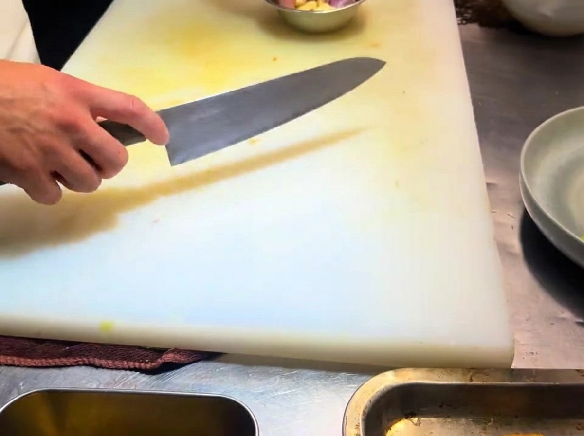 Thinly sliced garlic cloves spread out on a white cutting board.