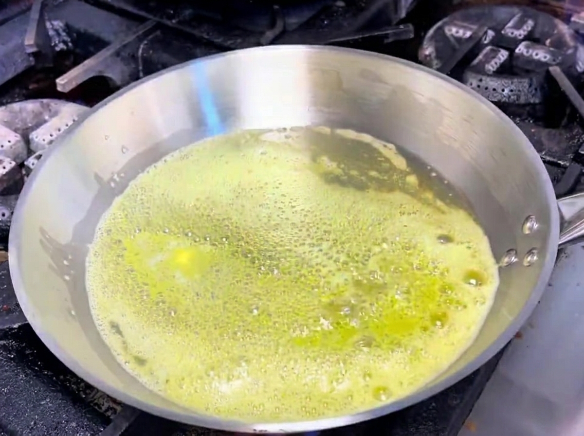 Garlic and shallots sizzling in melted butter within a stainless steel pan.