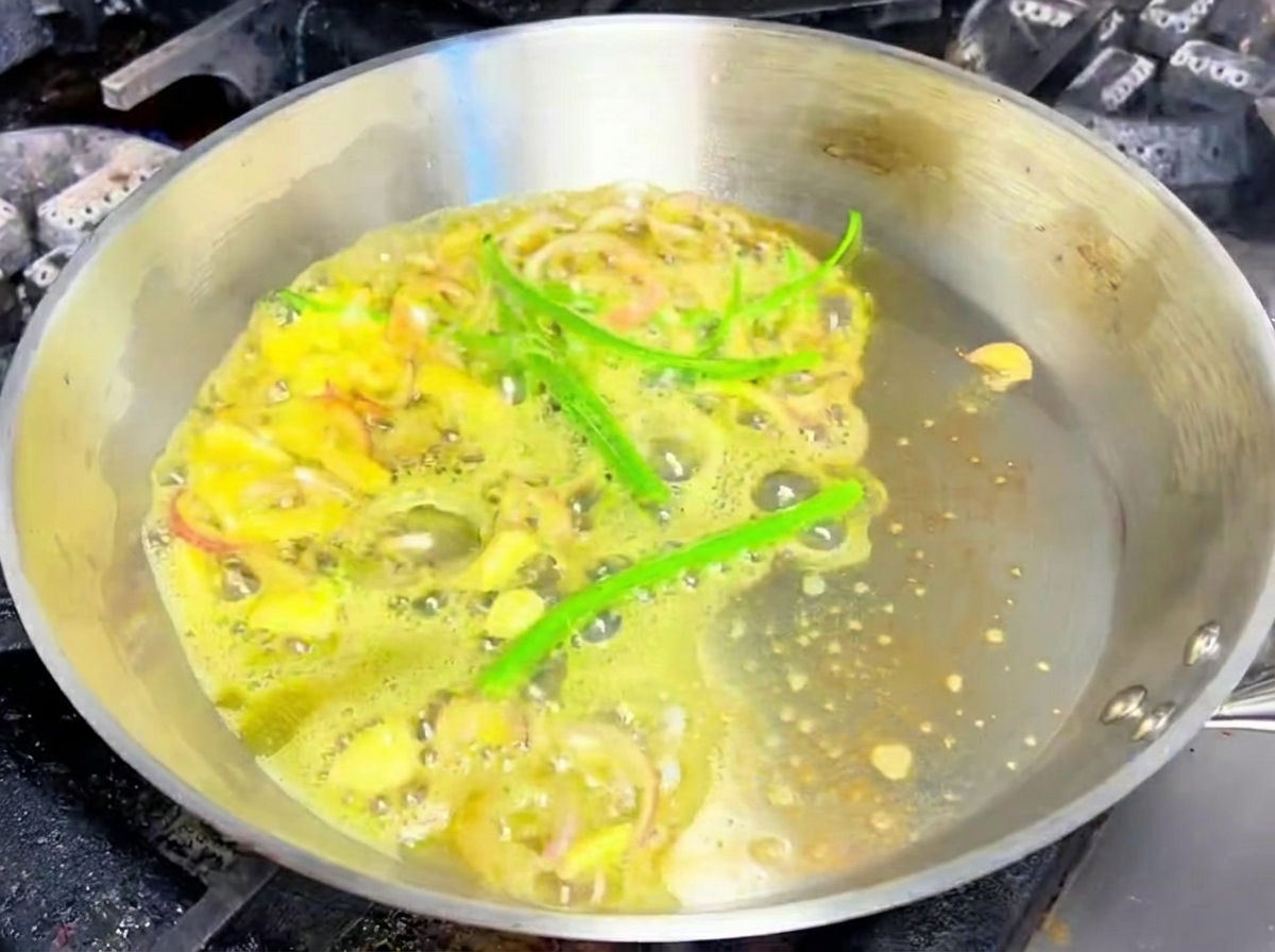 Sliced garlic, shallots, and green chili peppers sizzling in melted butter in a stainless steel pan.