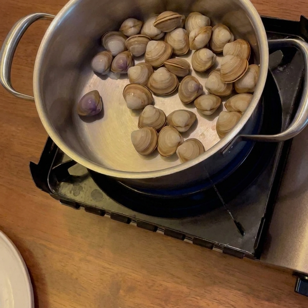 Alcohol being poured into a pot with clams, potatoes, and carrots, which are sitting on a portable gas stove.