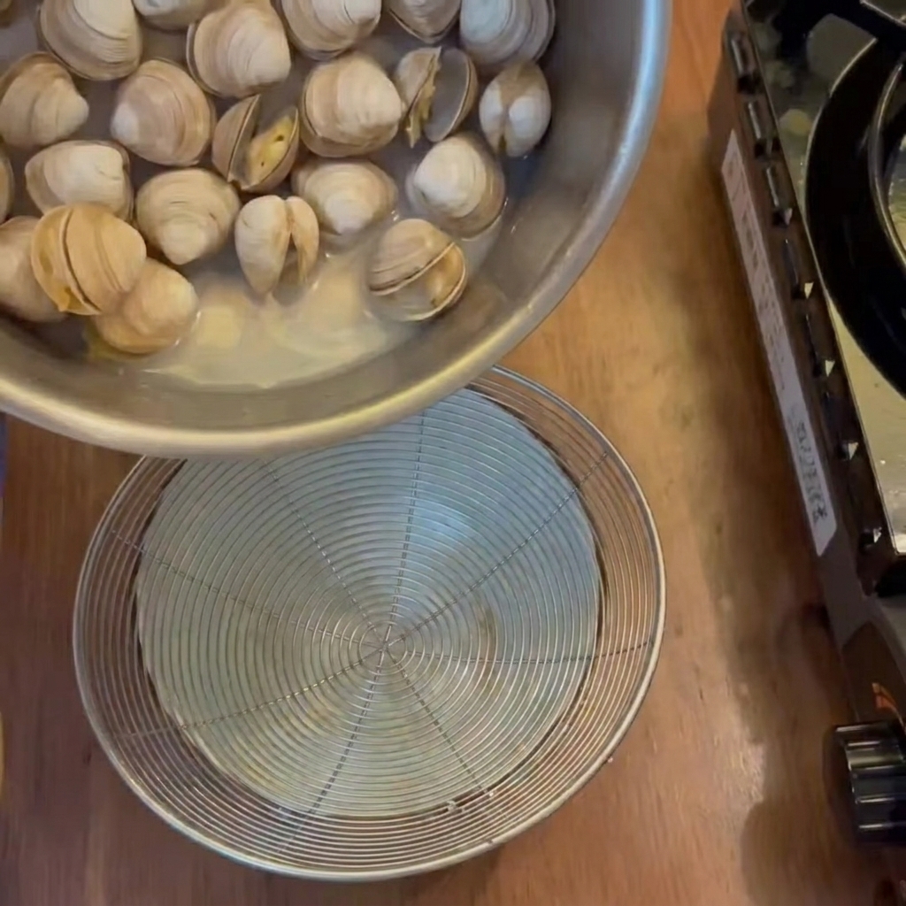 The liquid broth being strained from the cooked clams into a bowl below.