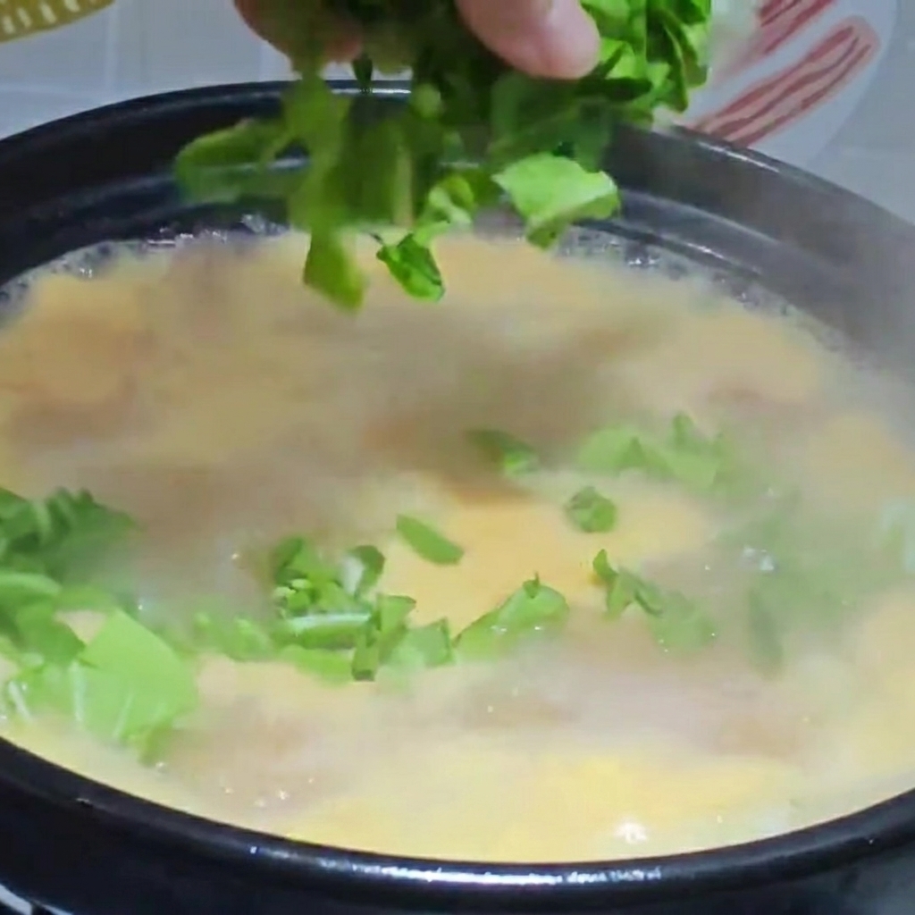 Chopped greens and shredded chicken being added to a finished pot of boiling dough drop soup.