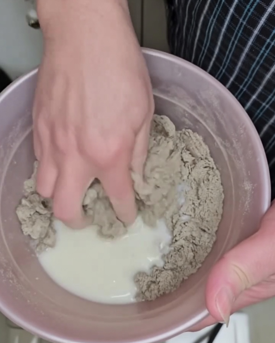 Buckwheat dough being kneaded by hand in a bowl, forming small irregular drops.