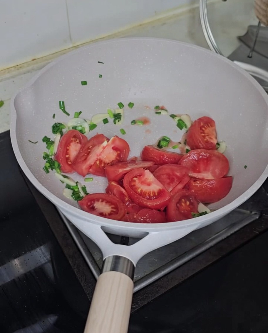 Fresh diced tomatoes being added to the pan containing sautéed aromatics.