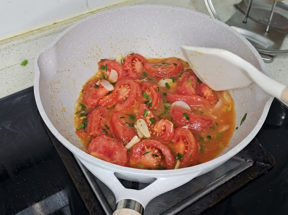 Boiling water being poured into the pan over the stir-fried tomatoes.