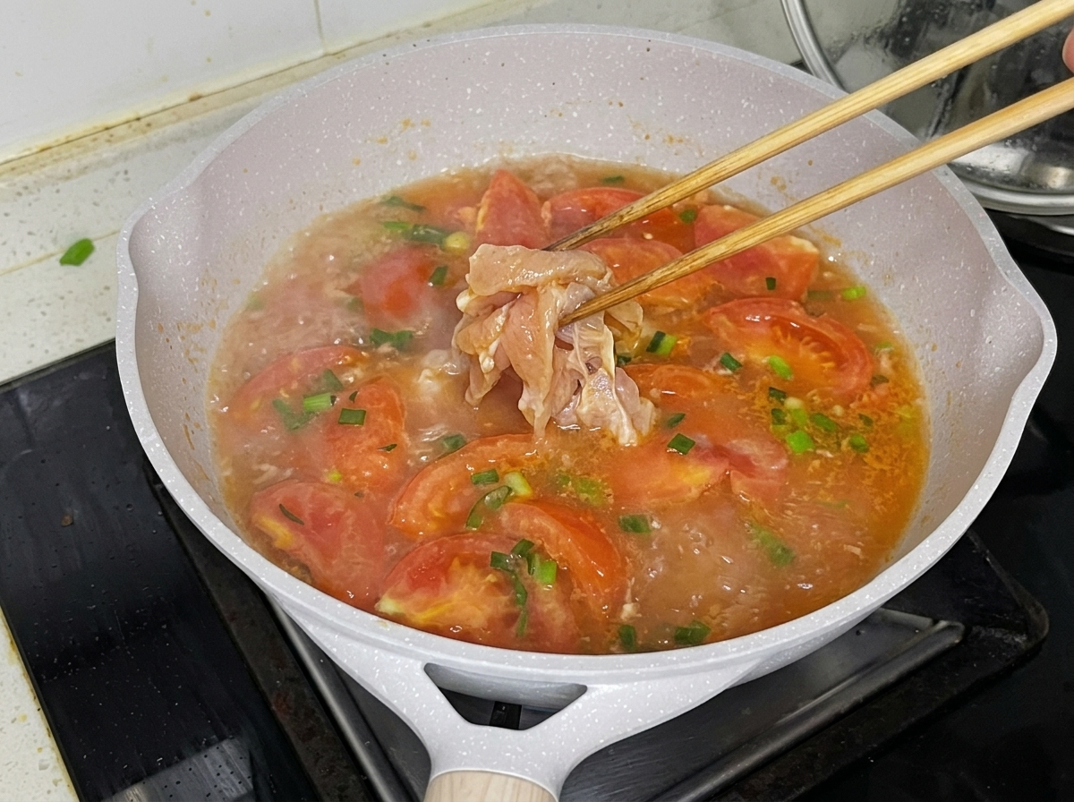 Chicken breast pieces being carefully dropped into the simmering tomato broth with chopsticks.